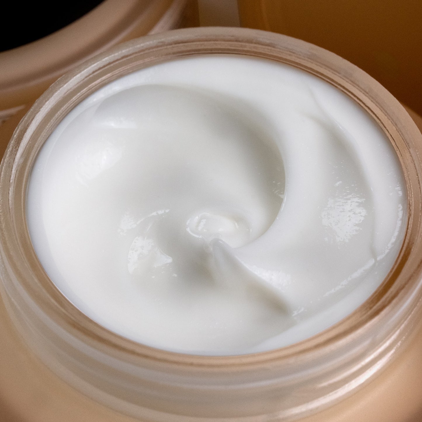 A close-up of a velvety white night repair therapy product swirled inside an amber jar.
