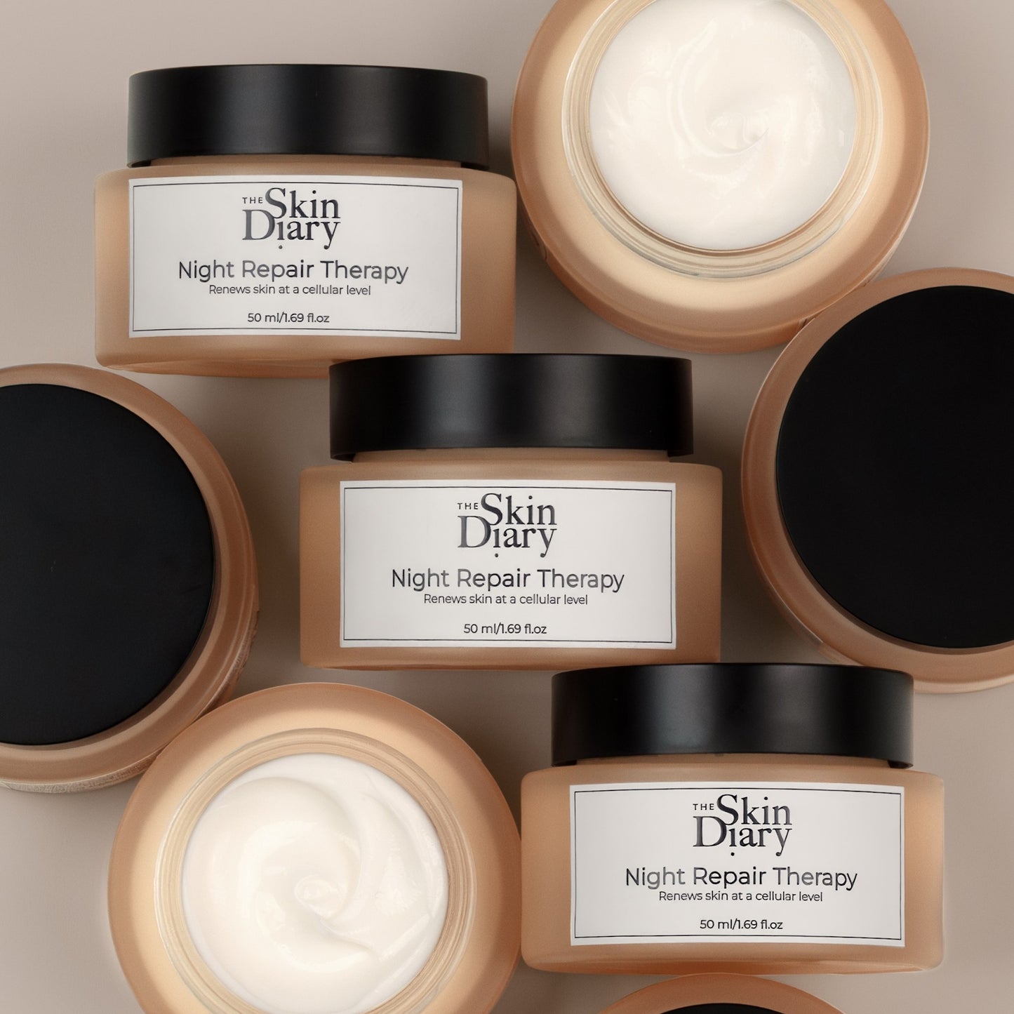 A collage of The Skin Diary Night Repair Therapy cream arranged on a light beige background, with two jars open to show the white cream inside and two closed. The jars are a warm amber colour with black lids and white labels.